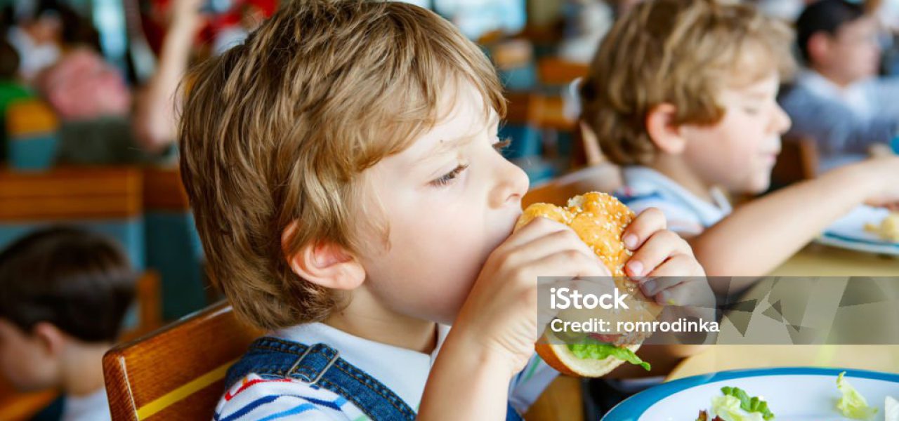 Cute healthy preschool kid boy eats hamburger sitting in school or nursery cafe. Happy child eating healthy organic and vegan food in restaurant. Childhood, health concept