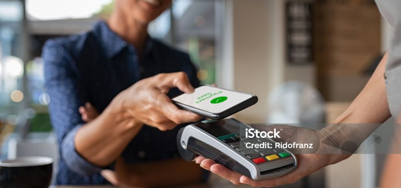 Mature woman paying bill through smartphone using NFC technology in a restaurant. Satisfied customer paying through mobile phone using contactless technology. Close up hands of mobile payment at a coffee shop.